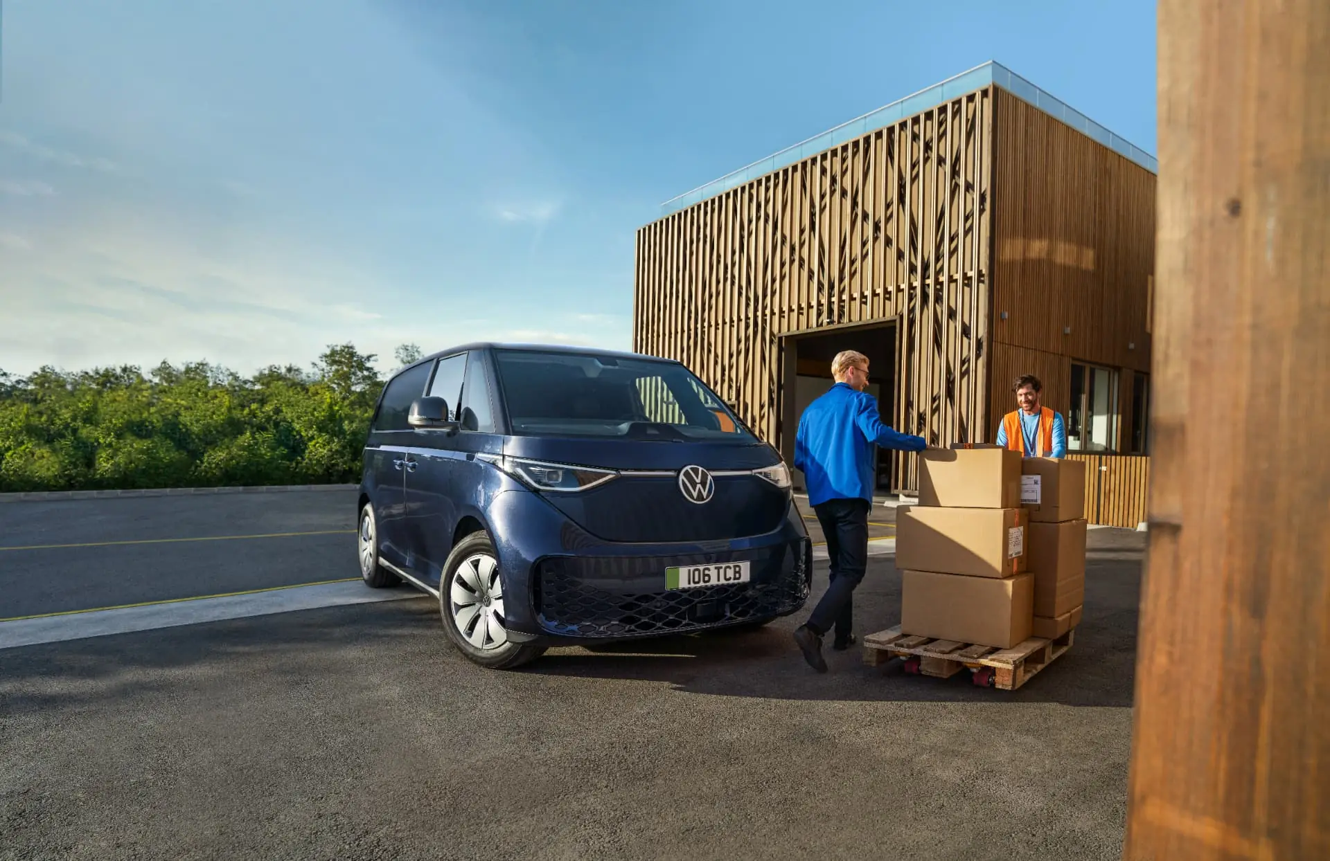Driver loading boxes into a dark blue Volkswagen ID. Buzz Cargo outside a depot