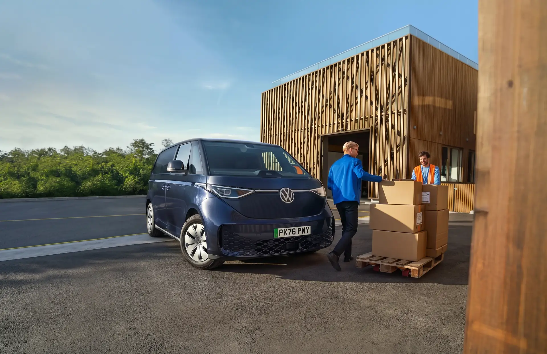 Driver loading boxes into a dark blue Volkswagen ID. Buzz Cargo outside a depot